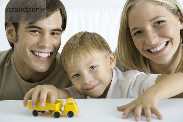 Familie lächelt in die Kamera  Junge spielt mit Spielzeugwagen