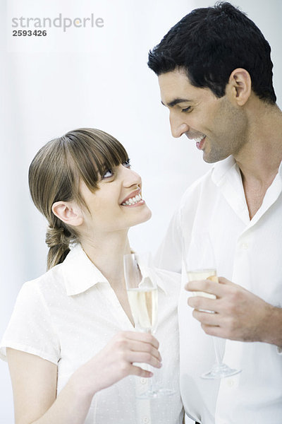 Ein Paar hält Gläser Champagner und lächelt sich an.