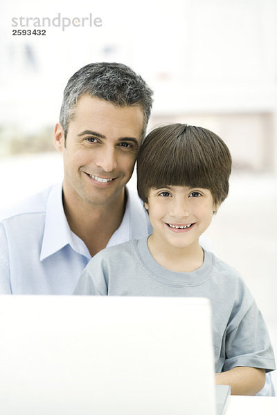 Vater und Sohn sitzend mit Laptop  lächelnd  Portrait