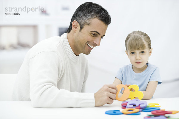 Vater und Tochter spielen mit Zahlenspielzeug  Mädchen schaut in die Kamera