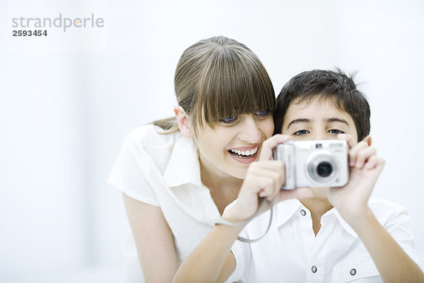 Junge fotografiert mit Kamera  Mutter lehnt sich über die Schulter  lächelt