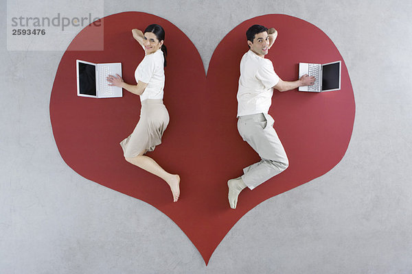 Mann und Frau liegen auf großer Herzgrafik  beide mit Laptop-Computer