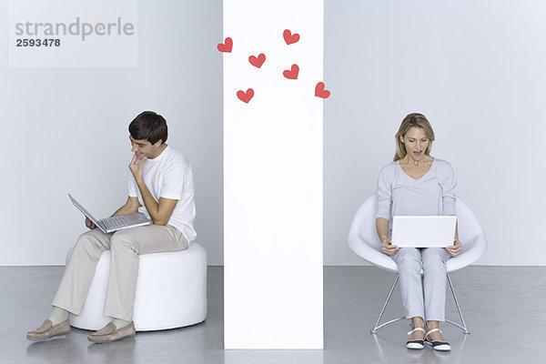Mann und Frau benutzen Laptops  Herzen schweben in der Luft zwischen ihnen.
