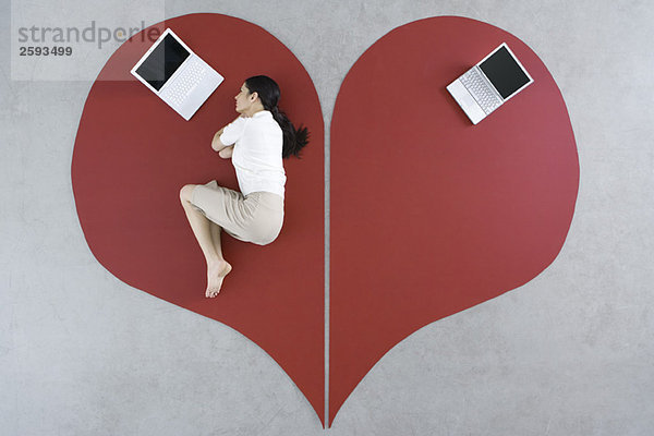 Frau auf dem Boden liegend mit Laptop auf großem gebrochenem Herzen  verlassener Laptop hinter ihr