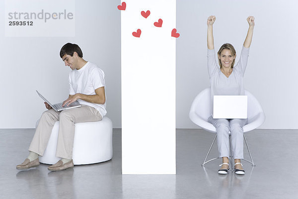 Mann und Frau benutzen Laptops  Herzen schweben zwischen ihnen  die Arme der Frau erhoben.