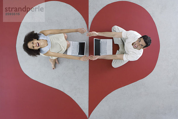 Mann und Frau sitzen mit Laptops auf großem Herzen  Arme ausstrecken  Hände berühren  Draufsicht
