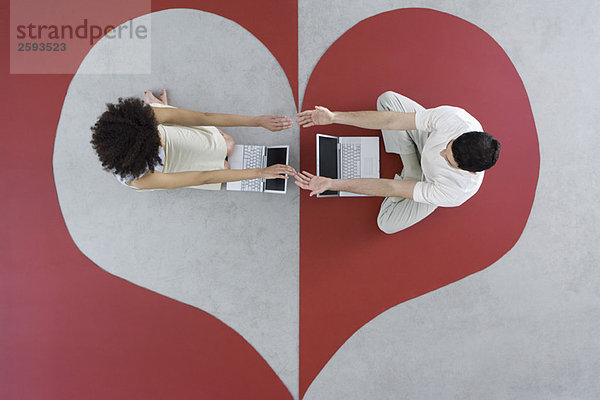 Mann und Frau sitzen mit Laptops auf großem Herzen  Arme ausstrecken  Hände berühren  Draufsicht