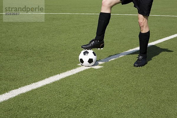 Ein junger Mann auf einem Fußballfeld mit dem Fuß auf einem Fußball  niedriger Abschnitt