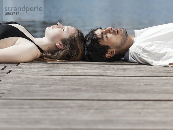 Ein junges Paar liegt auf einem Steg Kopf an Kopf.