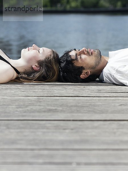 Ein junges Paar liegt auf einem Steg Kopf an Kopf.