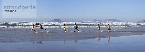 Leute  die an einem Strand entlanglaufen.