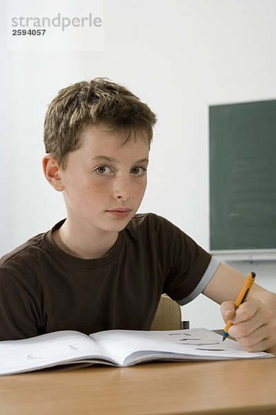 Ein vorpubertärer Junge  der in einem Klassenzimmer studiert.
