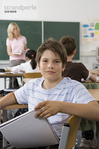 Ein vorpubertärer Junge sitzt hinten im Klassenzimmer und schaut in die Kamera.