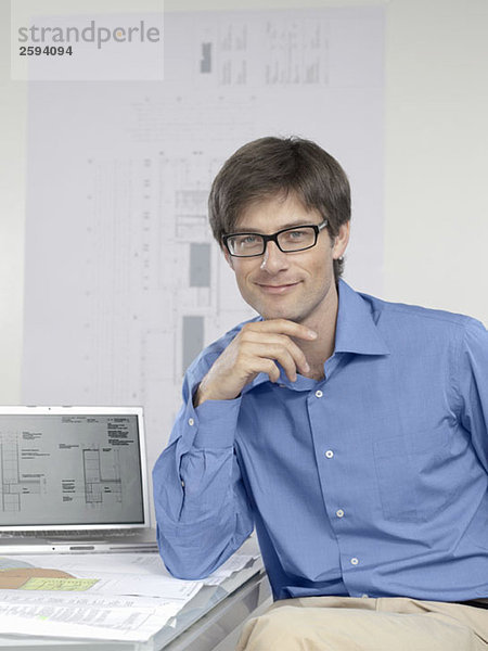 Ein Architekt am Schreibtisch mit Laptop und Architekturzeichnungen