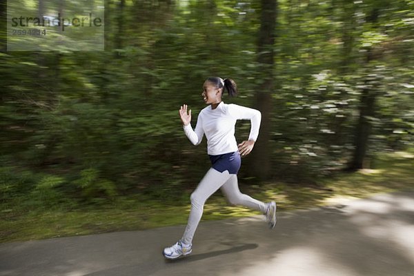 Eine Frau  die durch einen bewaldeten Park joggt.