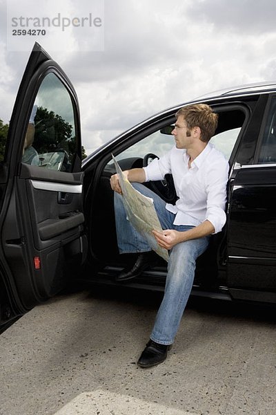 Ein Mann sitzt in einem Auto mit offener Tür und liest eine Karte.