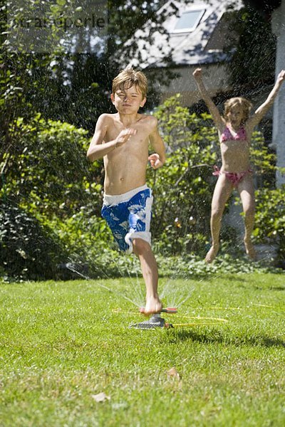 Zwei Kinder spielen in einer Sprinkleranlage