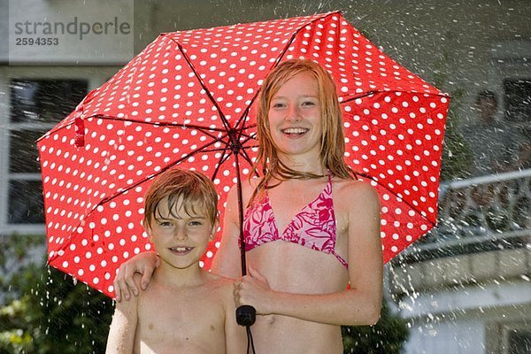 Zwei Kinder stehen unter einem Regenschirm in ihren Badeanzügen.