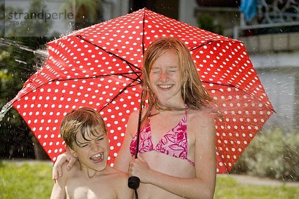 Zwei Kinder  die unter einem Regenschirm stehen und vom Spritzwasser getroffen werden.