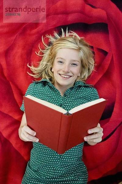 Ein Mädchen  das auf einer Decke liegt und ein Buch liest.