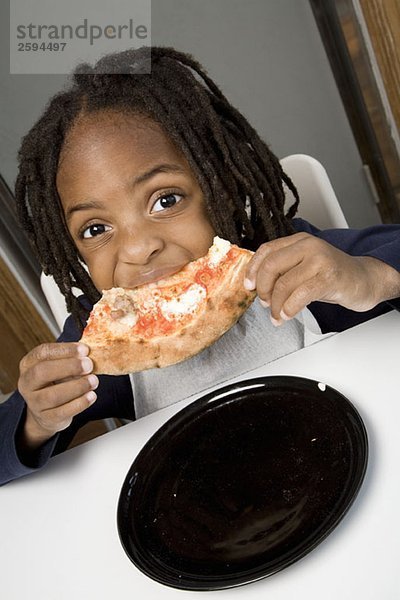 Ein kleiner Junge  der ein Stück Pizza isst.