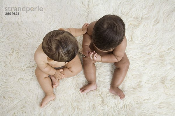 Zwei Babys sitzen auf einem Schaffellteppich  direkt darüber.