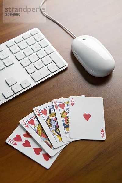 Ein Royal Flush-Pokerblatt auf einem Tisch neben einer Tastatur und einer Computermaus.