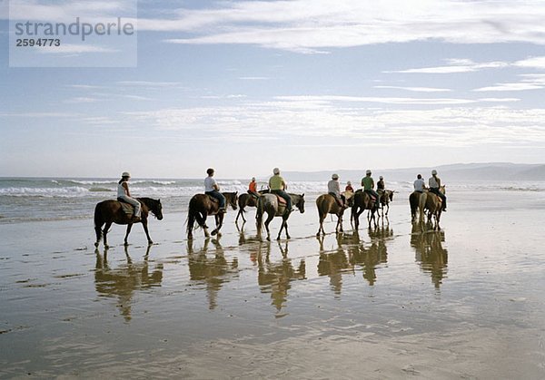 Eine Gruppe von Leuten  die am Strand reiten.