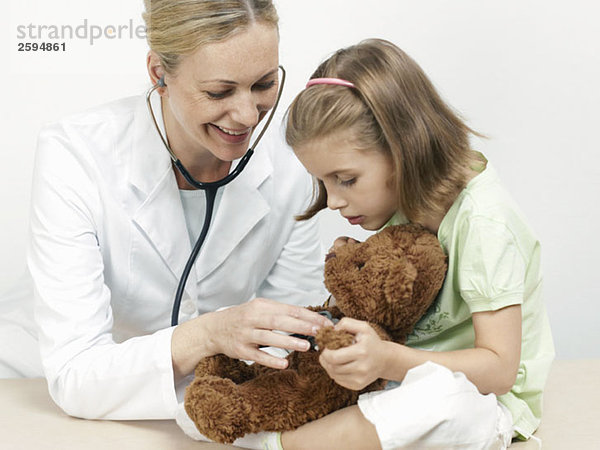 Eine Kinderärztin untersucht den Teddybär eines Mädchens.