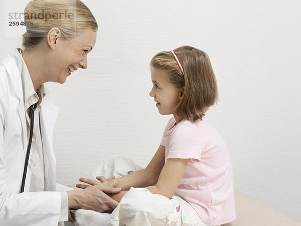 Ein Mädchen auf einem Untersuchungstisch mit Blick auf einen Kinderarzt und lächelndem Gesicht
