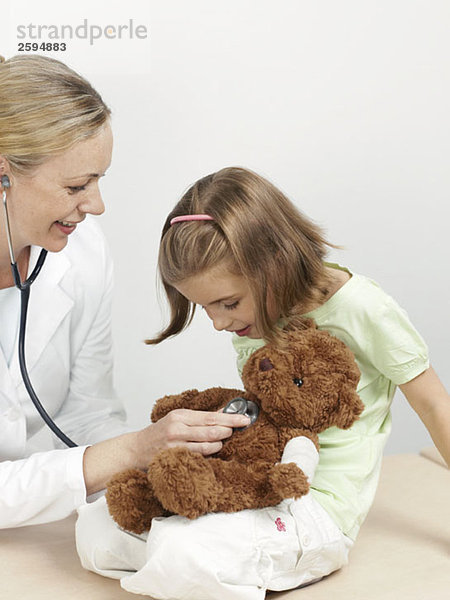 Eine Kinderärztin untersucht den Teddybär eines Mädchens.