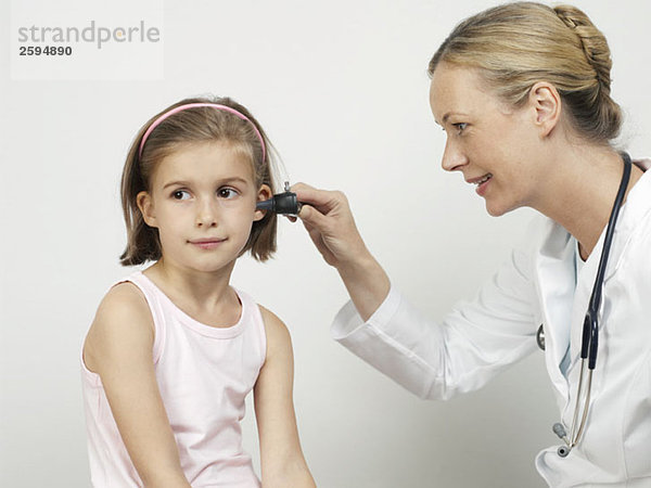 Eine Kinderärztin benutzt ein Otoskop  um das Ohr eines Mädchens zu untersuchen.