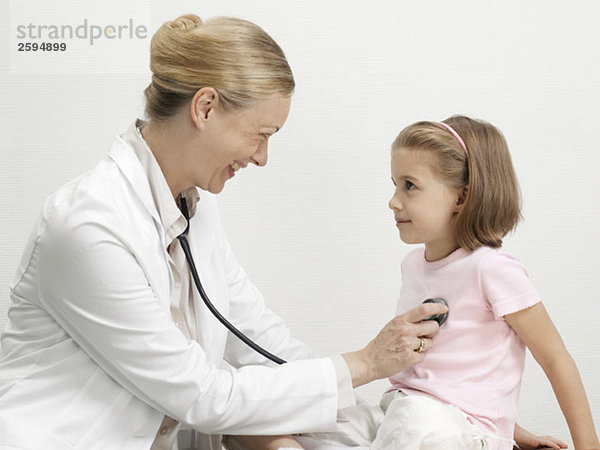 Eine Kinderärztin legt ein Stethoskop auf das Herz eines jungen Mädchens.