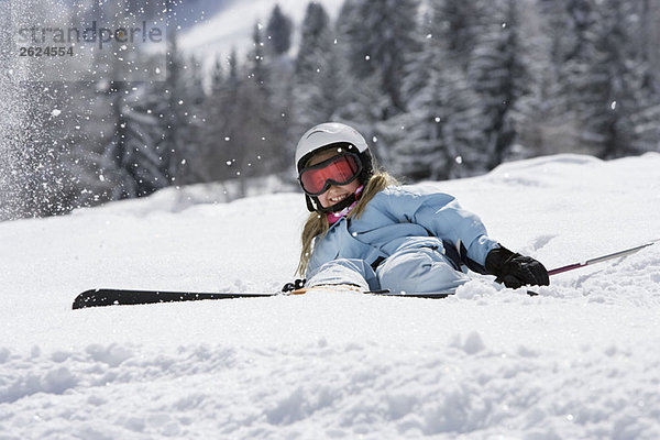 Mädchen mit Skiern auf Schnee liegend