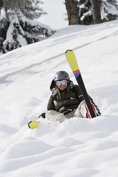 Frau im Schnee sitzend mit Skiern