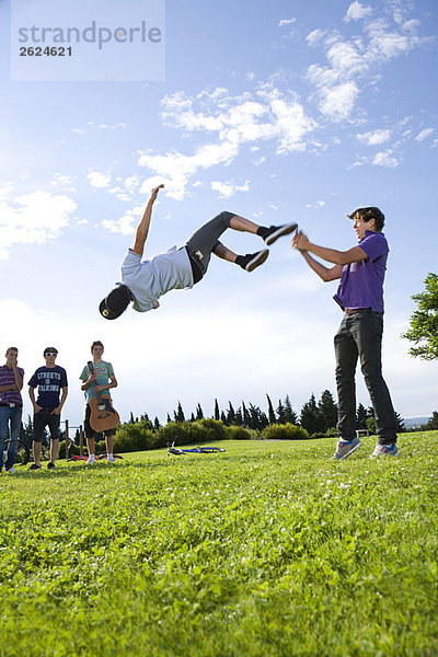 Teenager-Jungs helfen einem Freund  einen Flip zu machen.