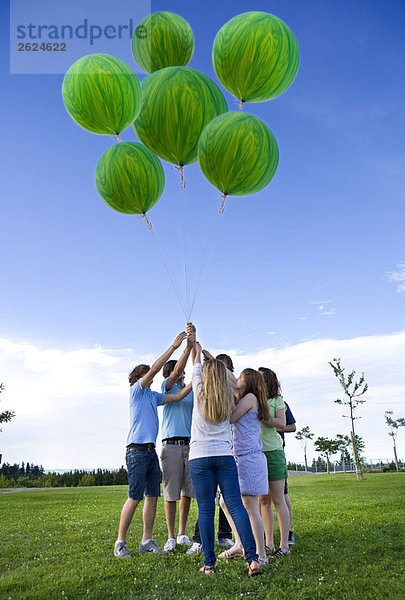 Jugendliche halten Helium-grüne Luftballons.