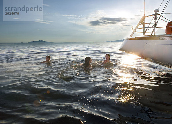 Drei Personen schwimmen neben dem Segelboot