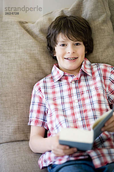 Junge auf einer Couch liegend  mit einem Buch