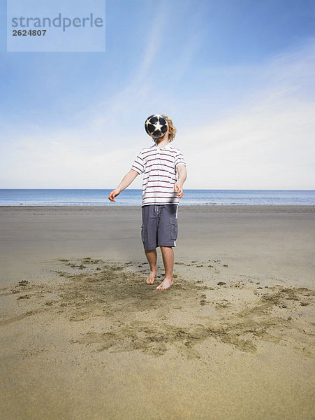 Junger Mann mit Fußball am Strand