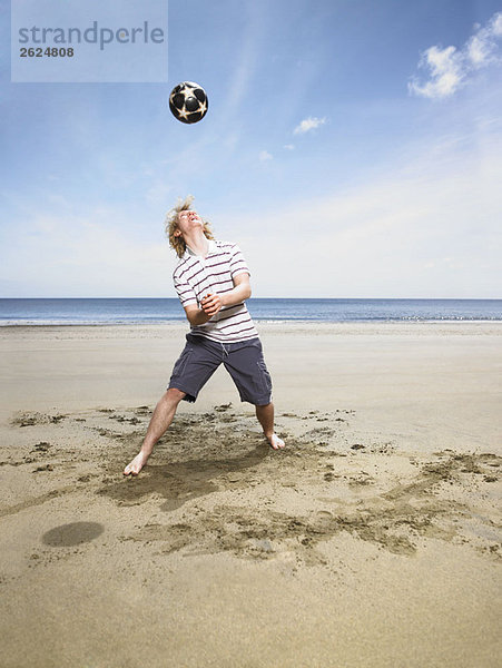 Junger Mann mit Fußball am Strand