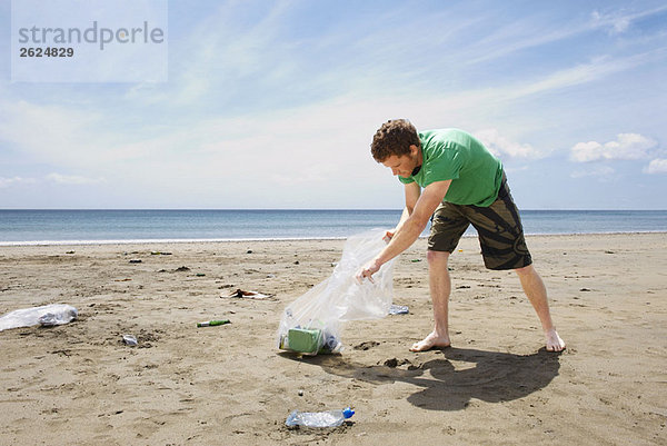 Junger Mann sammelt Müll am Strand
