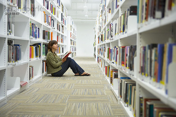 Junge Frau sitzt auf dem Boden der Bibliothek