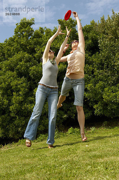 Zwei Frauen springen  um einen Frisbee zu fangen.