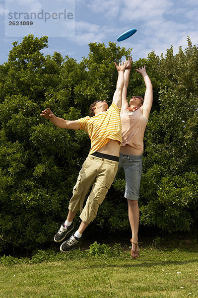 Ein Paar springt  um ein Frisbee zu fangen.