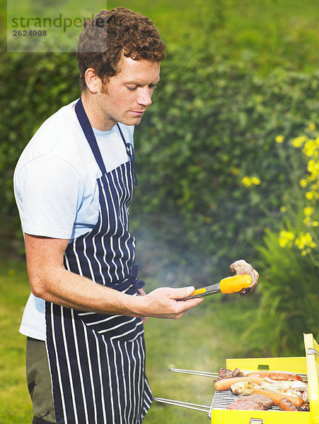 Mann inspiziert Lammkotelett beim Grillen