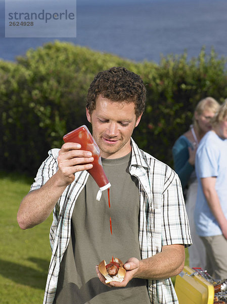 Mann gießt Ketchup auf Hot Dog