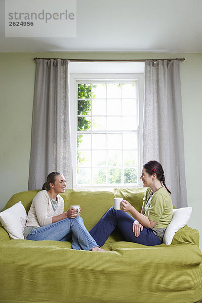 Zwei junge Frauen auf dem Sofa  mit Bechern