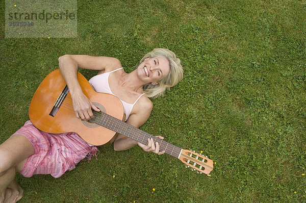 Frau auf Gras liegend  Gitarre spielend