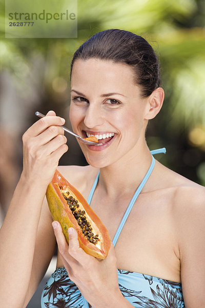 Junge Frau im Bikini  die eine Papaya löffelt.